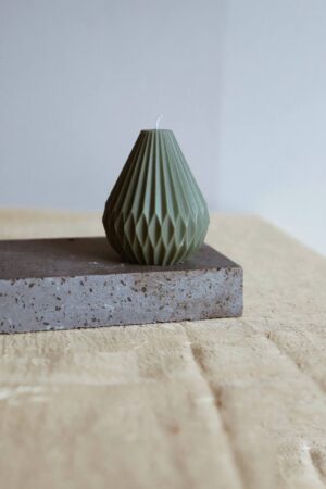 Candela artigianale "Drop" verde in cera naturale, design geometrico raffinato, posizionata su una base in pietra elegante